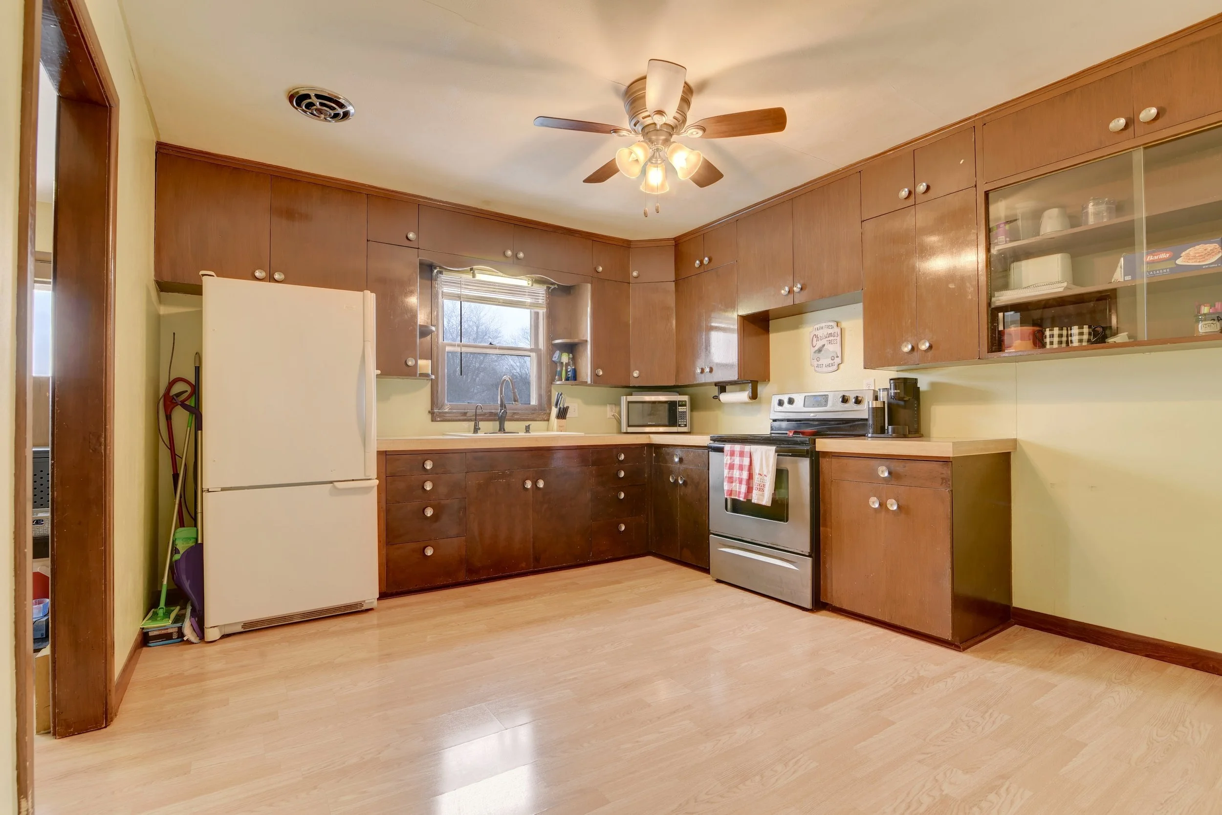 Kitchen with brown cabinets, white refrigerator, stove, microwave, and ceiling fan with lights.