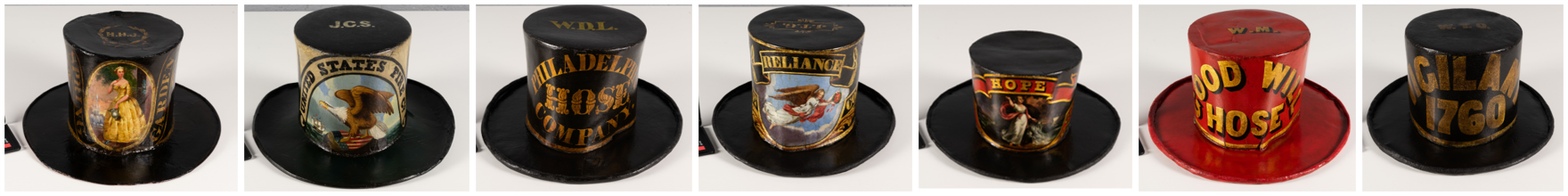 A series of 7 different fireman parade hats after treatment. Six of the hats are black and one is bright red. All have either text or images or both on them helping to denote which fire company the hat represents.