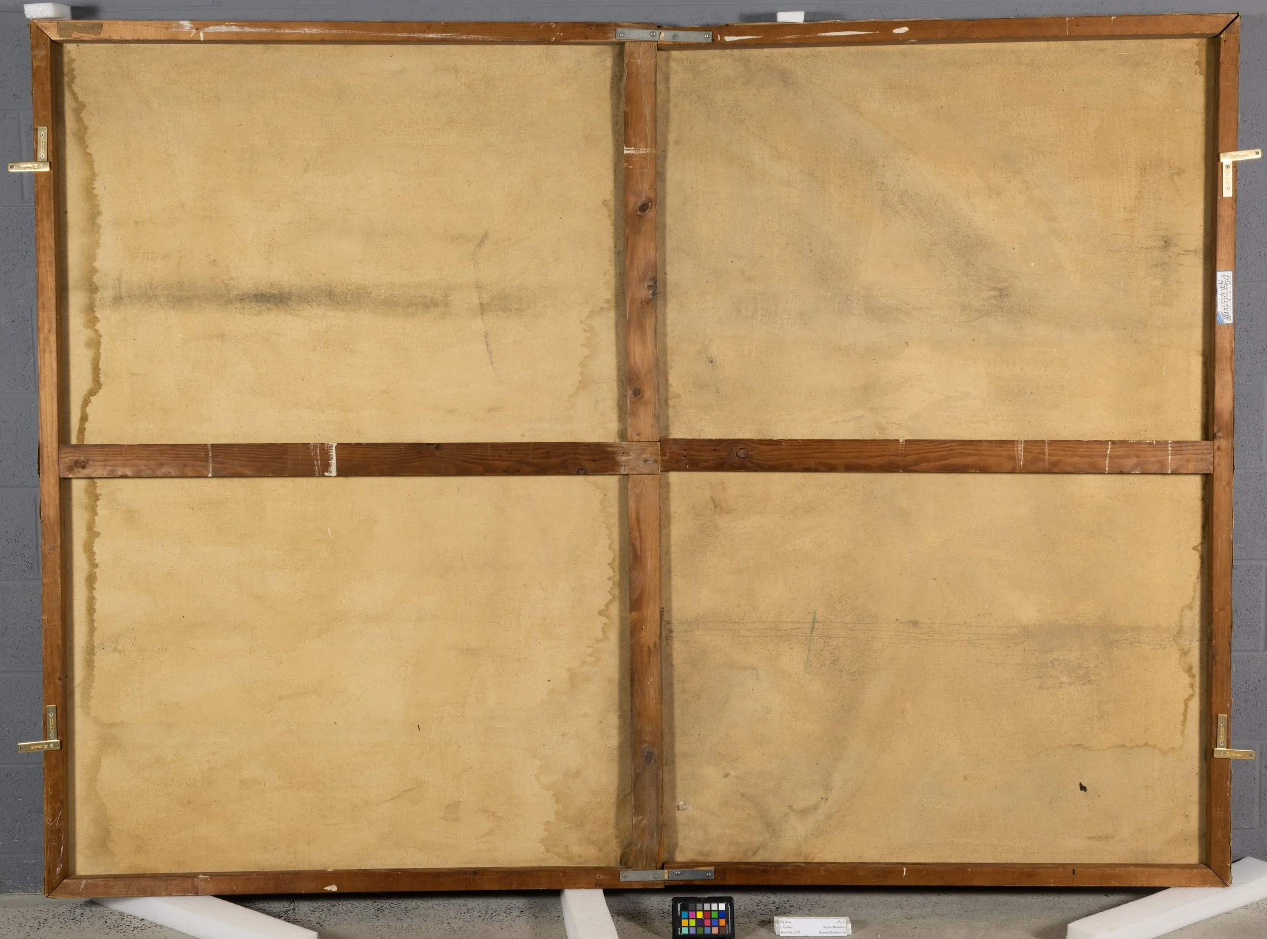 Close up of the back of a painting. There is a large brown stain in the middle of the canvas indicative of water damage