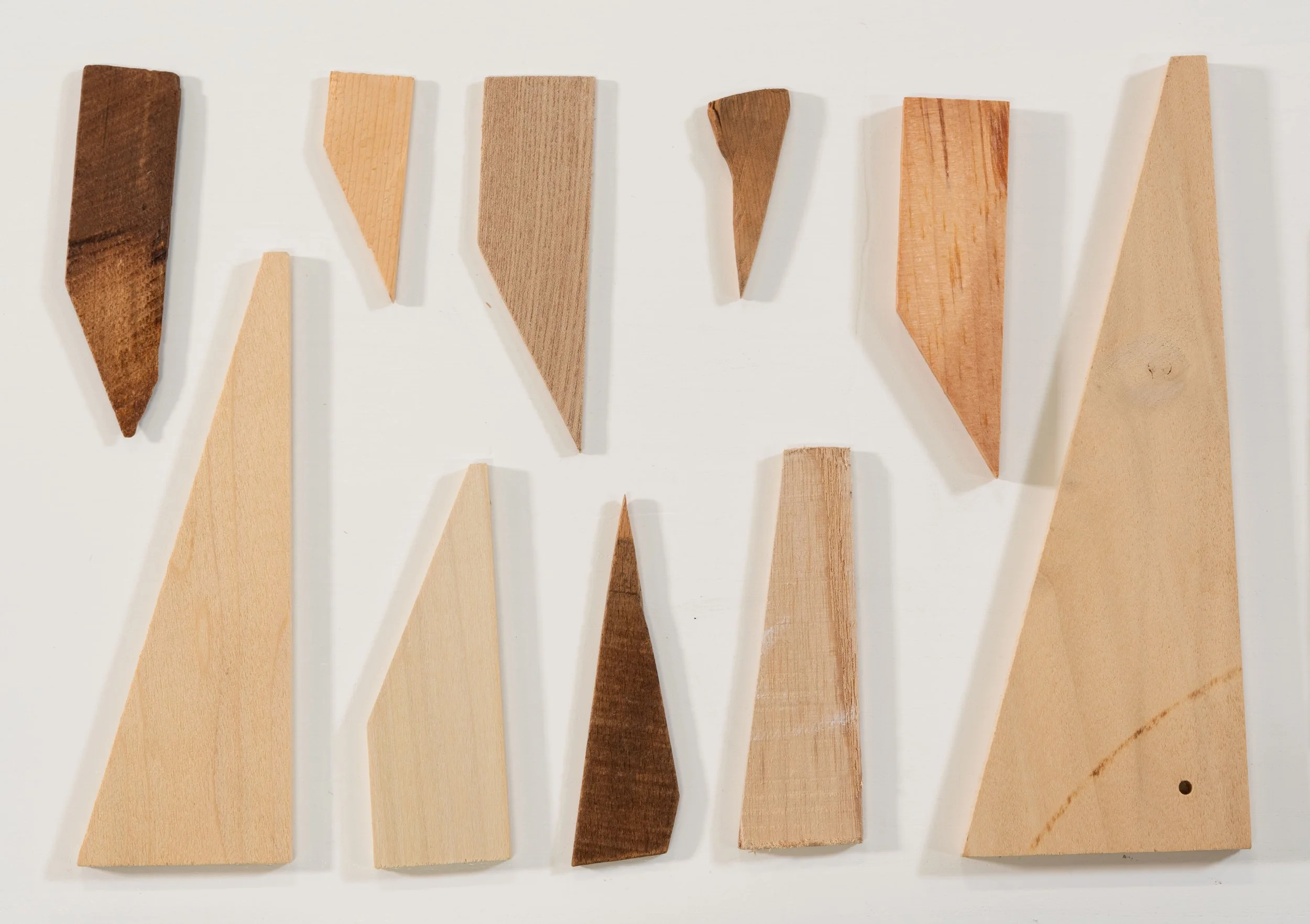 Examples of eight different wooden stretcher keys in various shapes and sizes, all in different shades of brown, on a white background