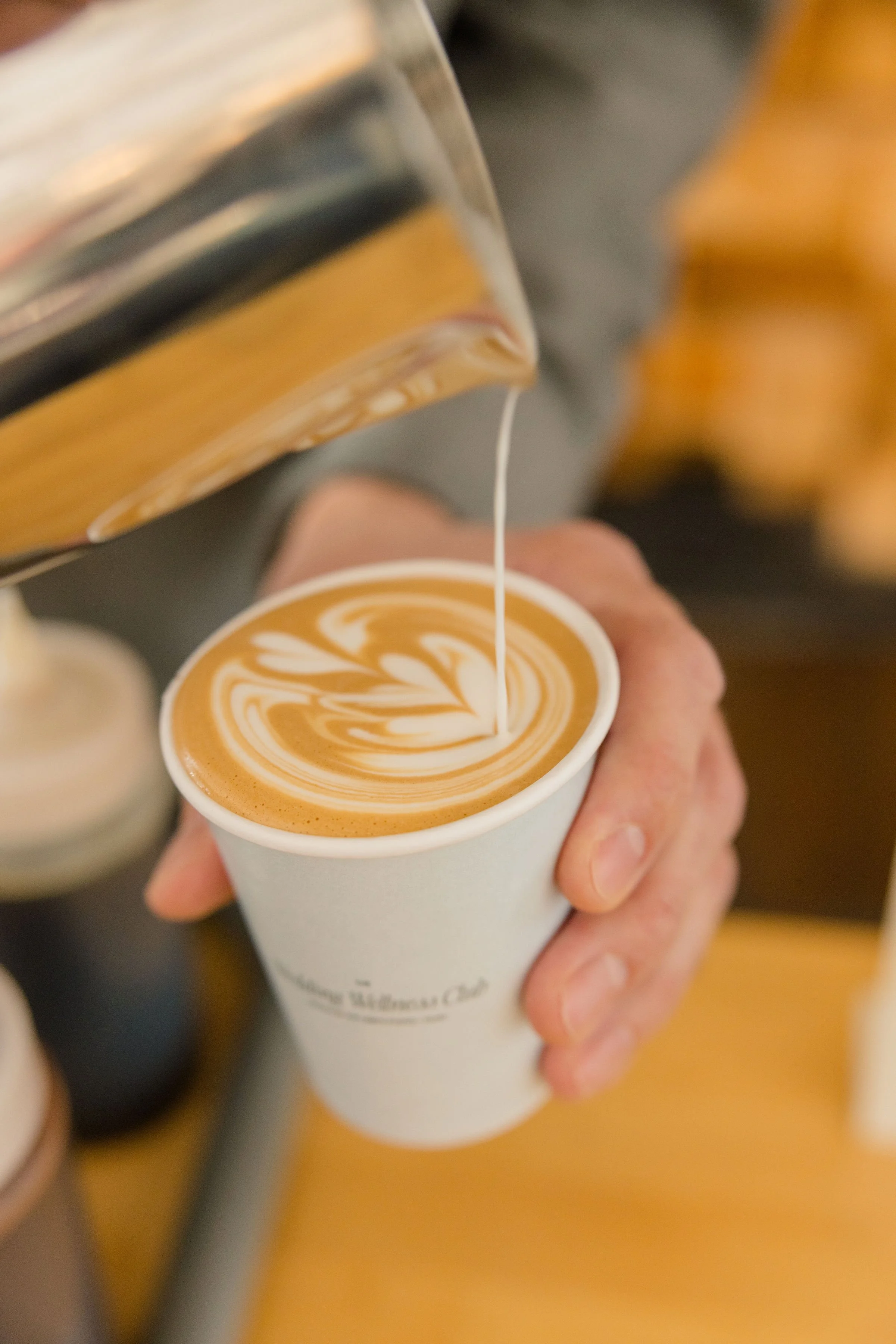 Barista pouring steamed milk into a cup of coffee, creating latte art with a heart design.