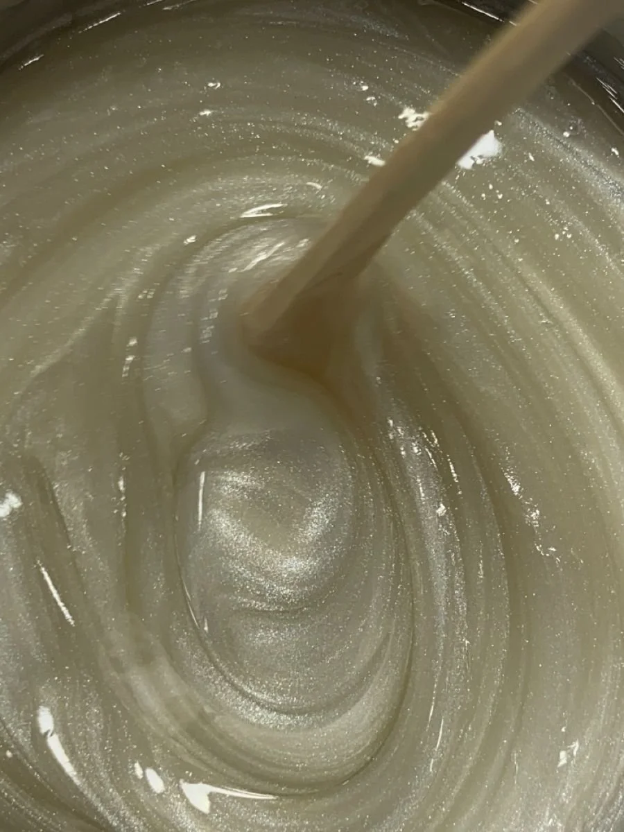 A close-up view of a creamy, soft wax being stirred in a wax pot.