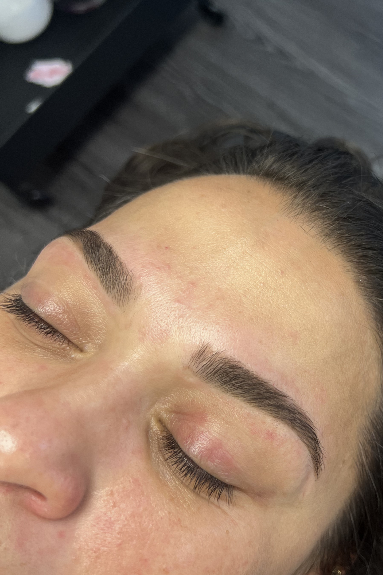 Close-up of a woman's face with freshly tinted eyebrows, eyes closed, showing smooth skin in an indoor setting.