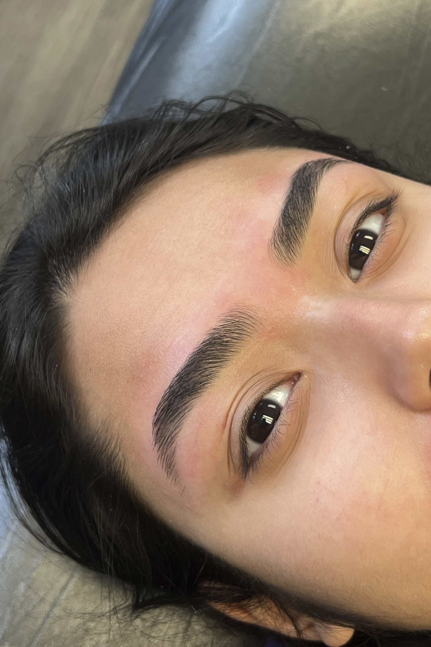 Close-up of a woman's face showing her eyebrows after an eyebrow wax, lying on a surface with a wooden floor in the background.