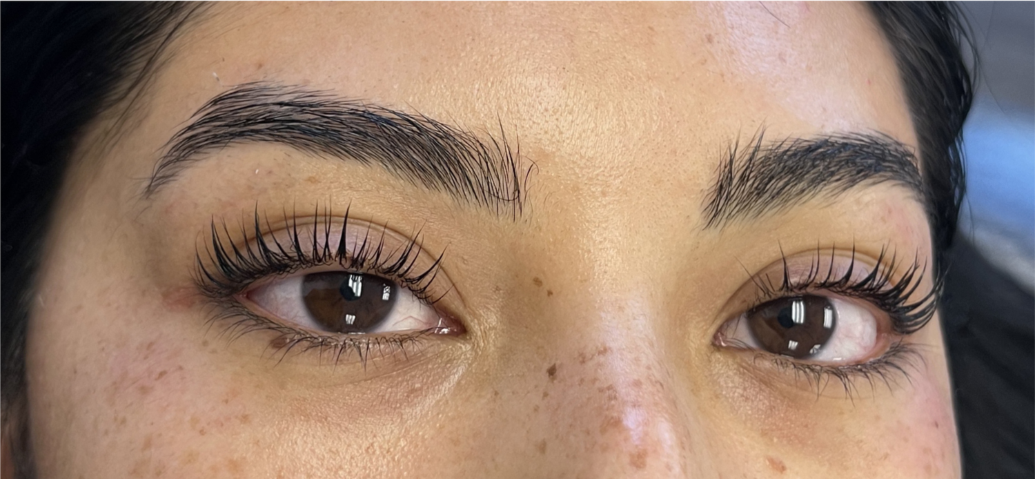Close-up of a woman's face, showing her eyebrows, eyes with a lash lift and tint, and some freckles on her nose and cheeks.