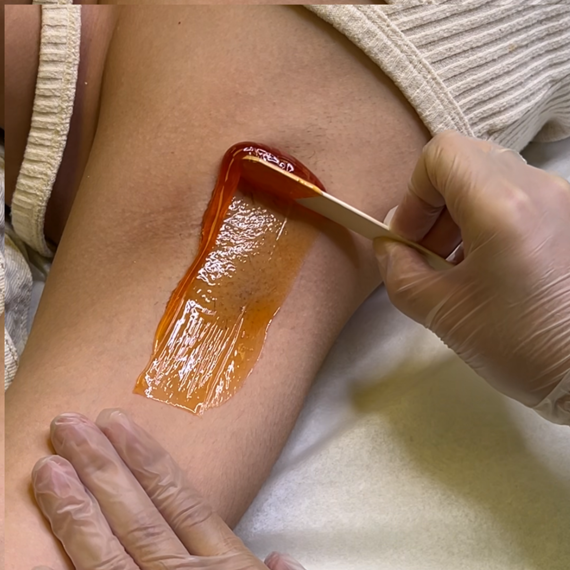 Person applying wax to their armpit for hair removal with a spatula.