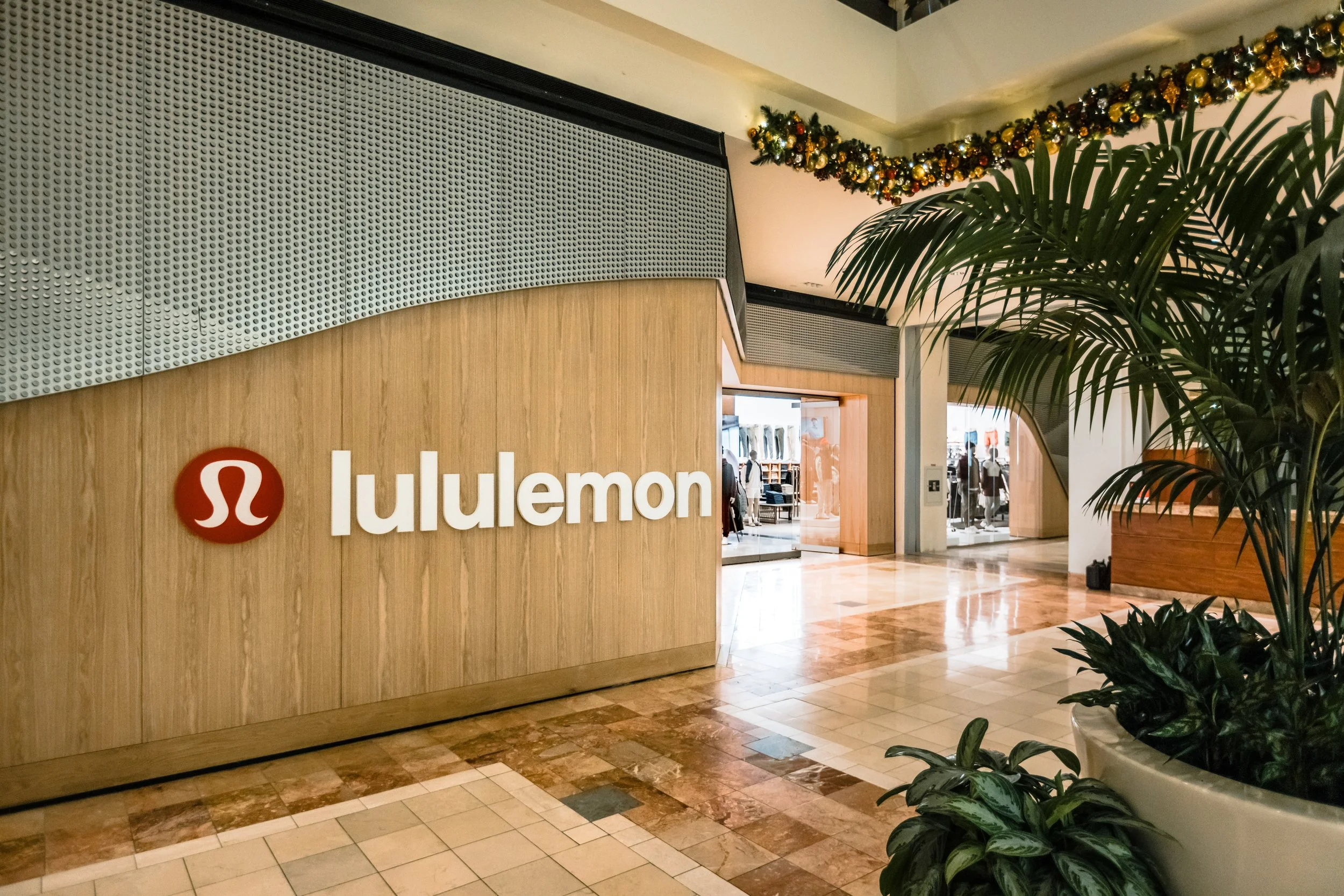 Lululemon store entrance decorated with holiday garland, with plants and tiled flooring inside a shopping mall
