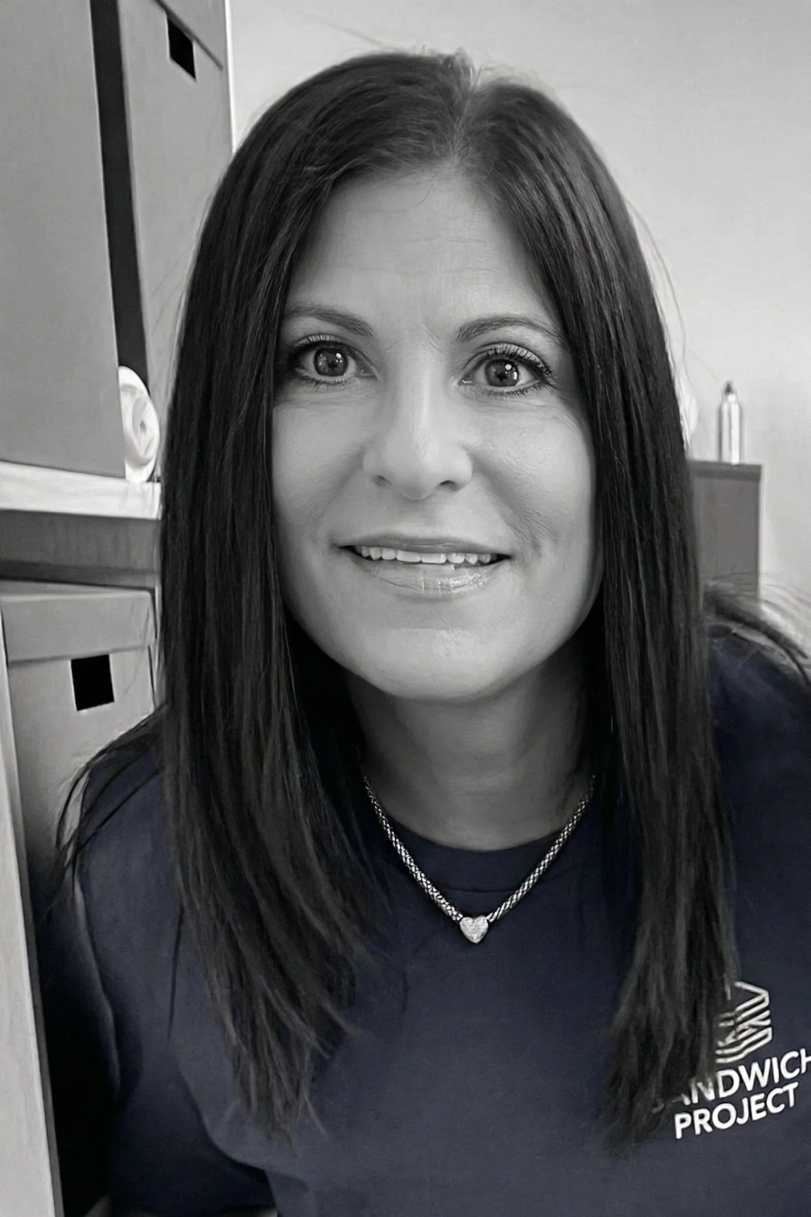 Black and white portrait of a woman smiling, with long dark hair, wearing a light top and a cardigan, against a plain background.