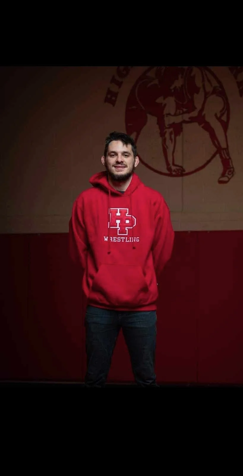A young man in a red hoodie with 'HP Wrestling' logo, standing in front of a wrestling-themed wall.