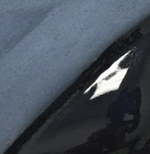 Close-up of a car with chipped paint and a visible scratch on the blue body, near a black painted surface.