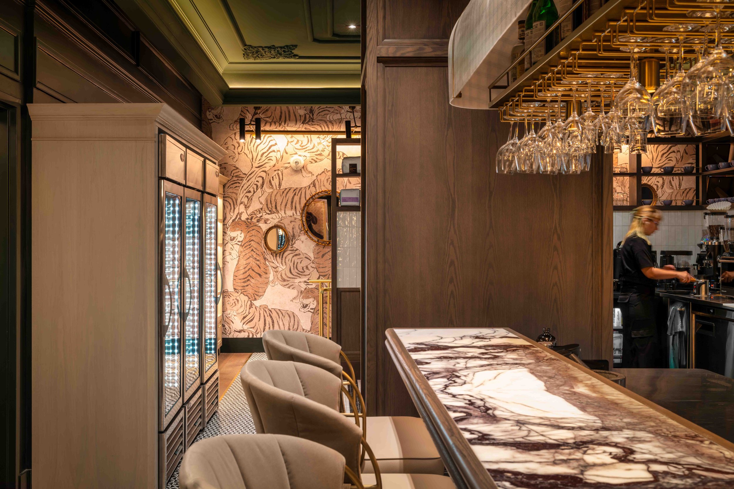 Luxurious bar interior with a marble countertop, hanging wine glasses, upholstered bar stools, and tiger wallpaper.