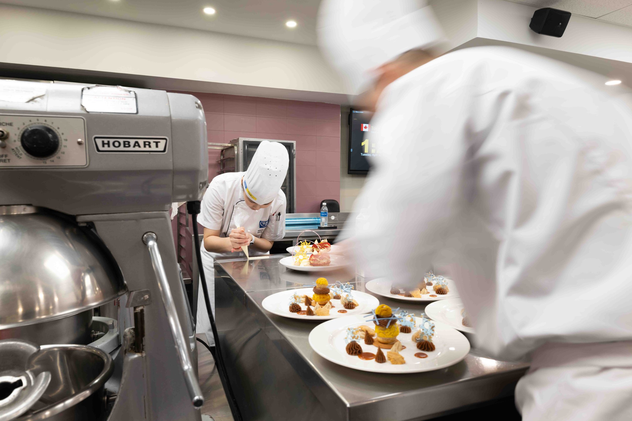 Chefs in a kitchen preparing decorative plates, with a Hobart mixer in the foreground.