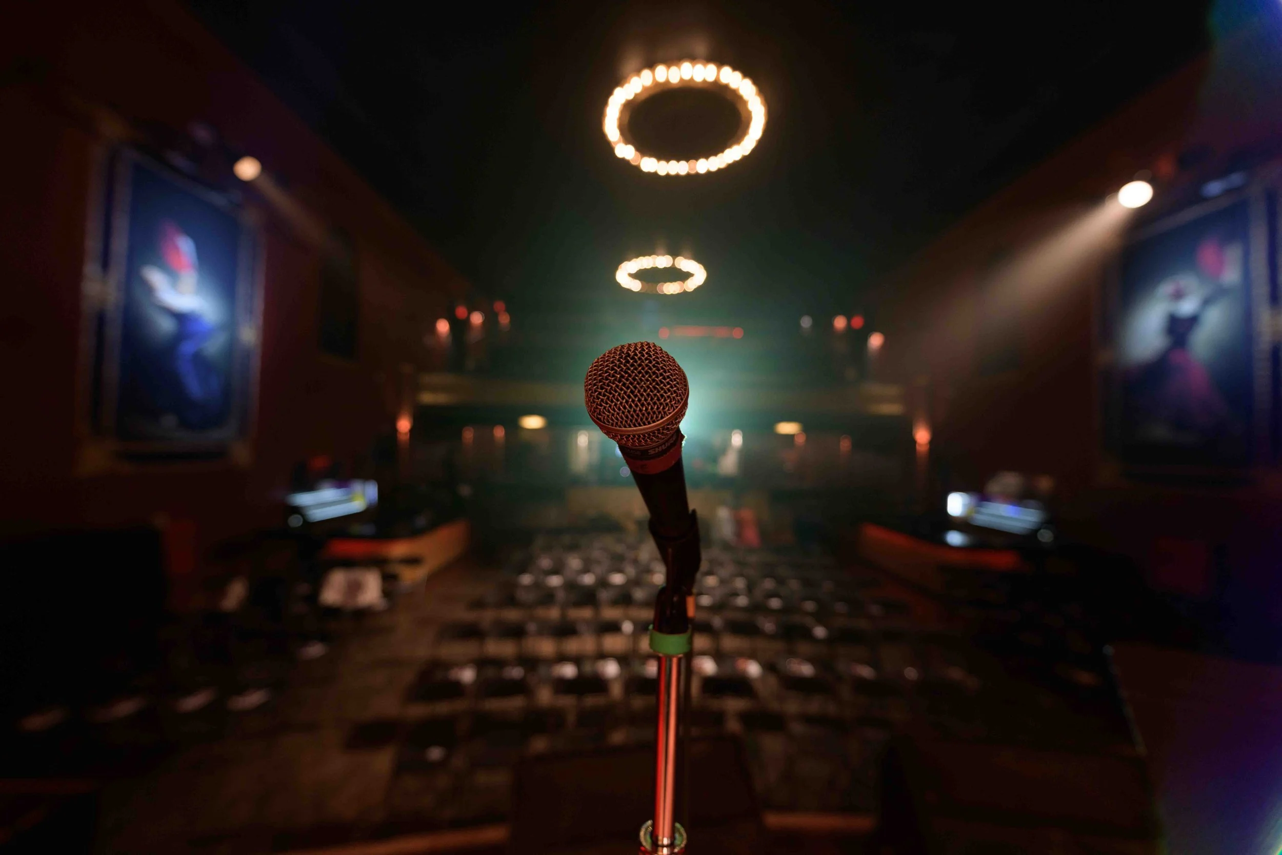 Microphone on a stand in an empty theater, with rows of chairs and dim lighting.