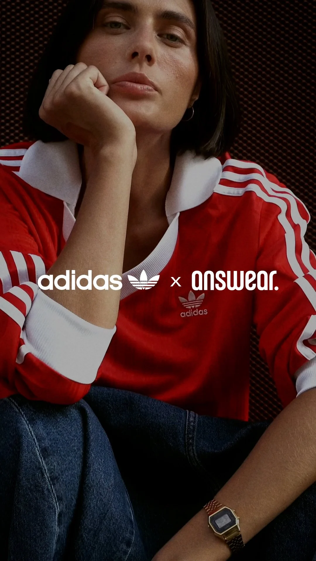 A person with medium skin tone and dark brown hair, dressed in a red and white Adidas jacket, sitting against a dark background, resting their chin on their hand, with a gold digital watch on their wrist.