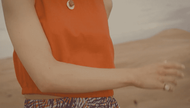 Close-up of a woman wearing an orange top and patterned pants, showing her arm and part of her waist, with a blurred background.
