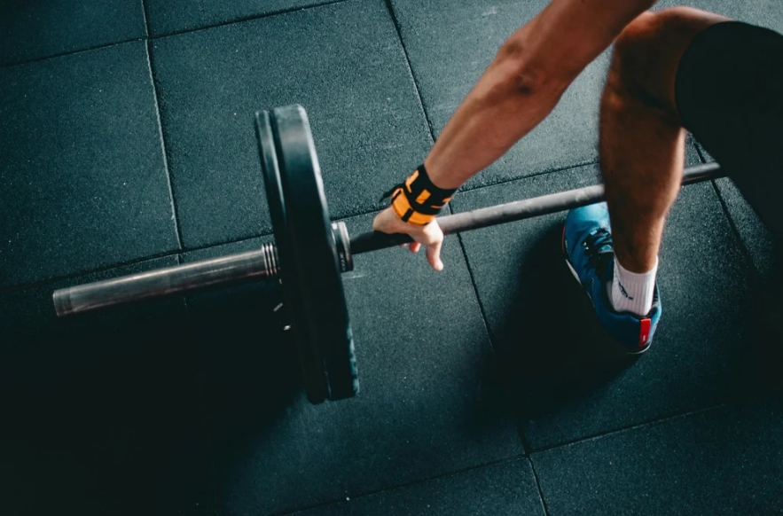 A person lifts a barbell on a gym floor, demonstrating strength training and fitness activity.