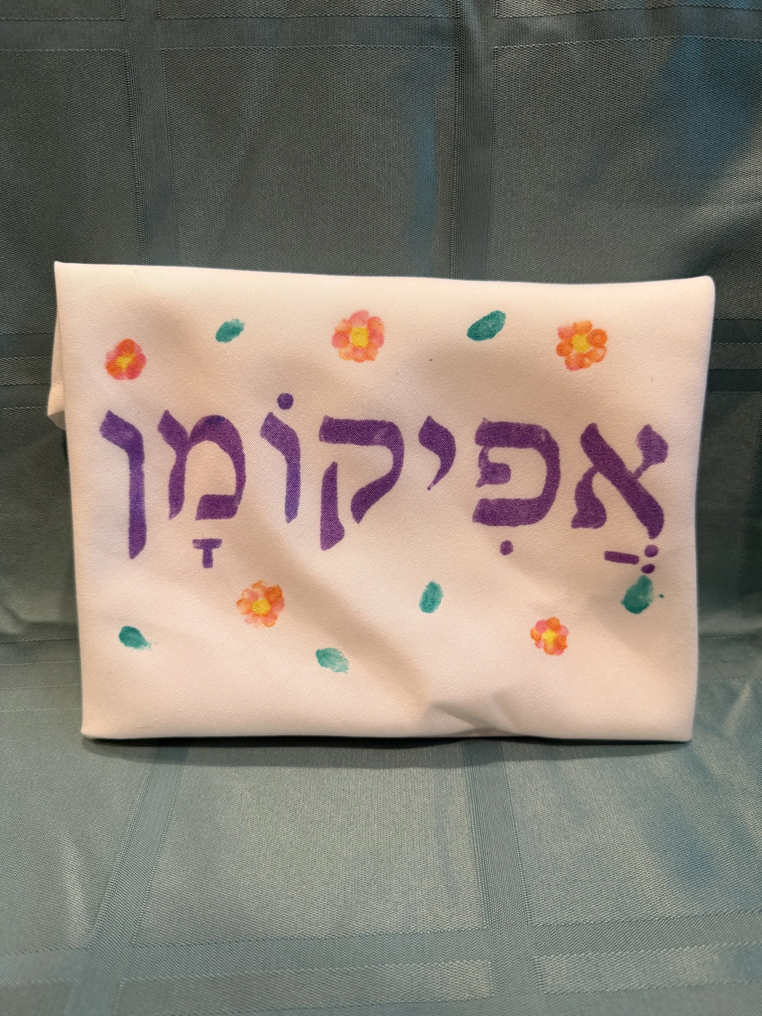 Create an afikoman bag with a cloth napkin, some fabric paint, and fabric glue/tape!