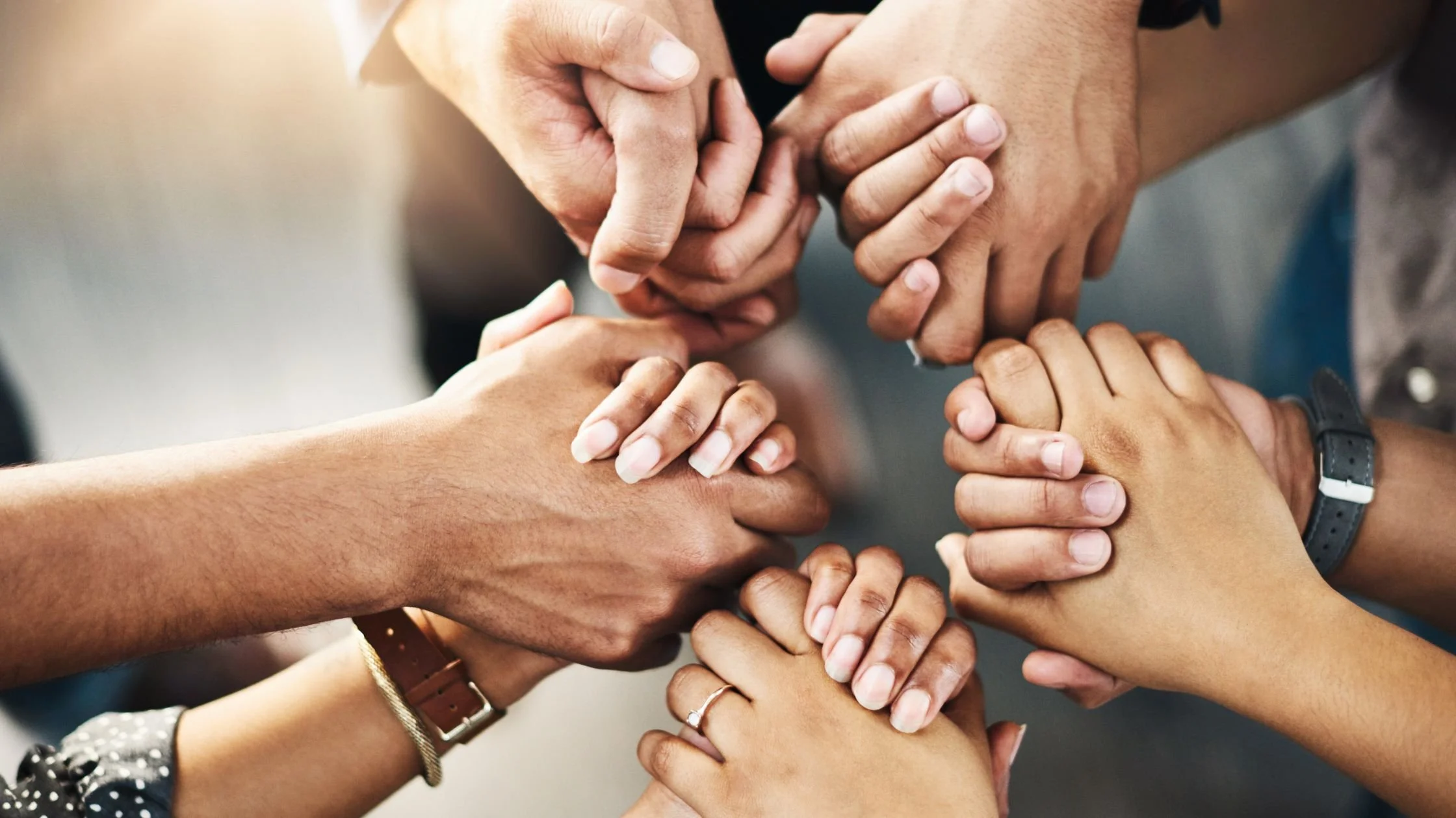 Picture of  5 pairs of clasped hands with different skin tones  in a circle