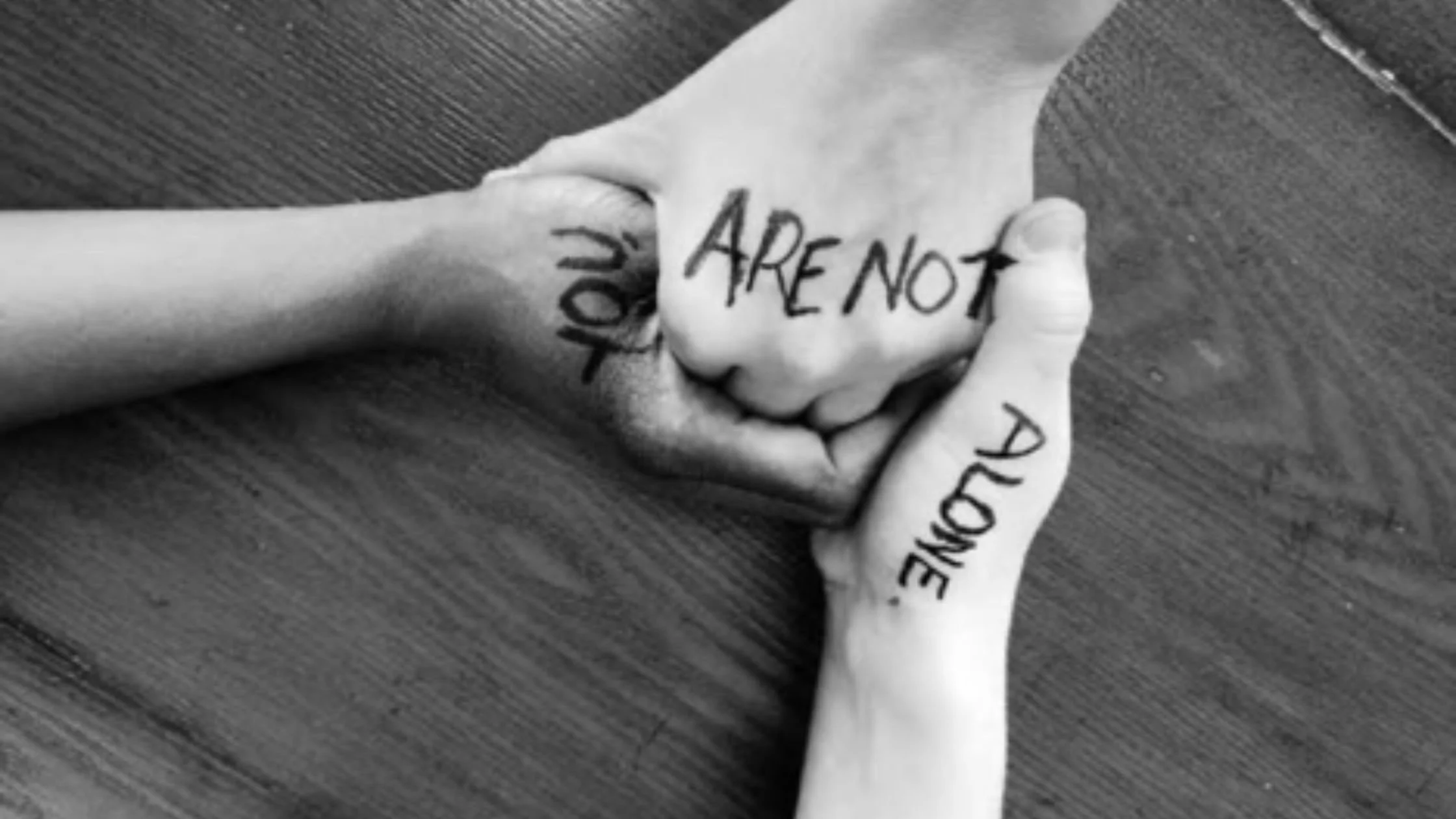 three hands clasped. The words "you are not alone" are written across the hands