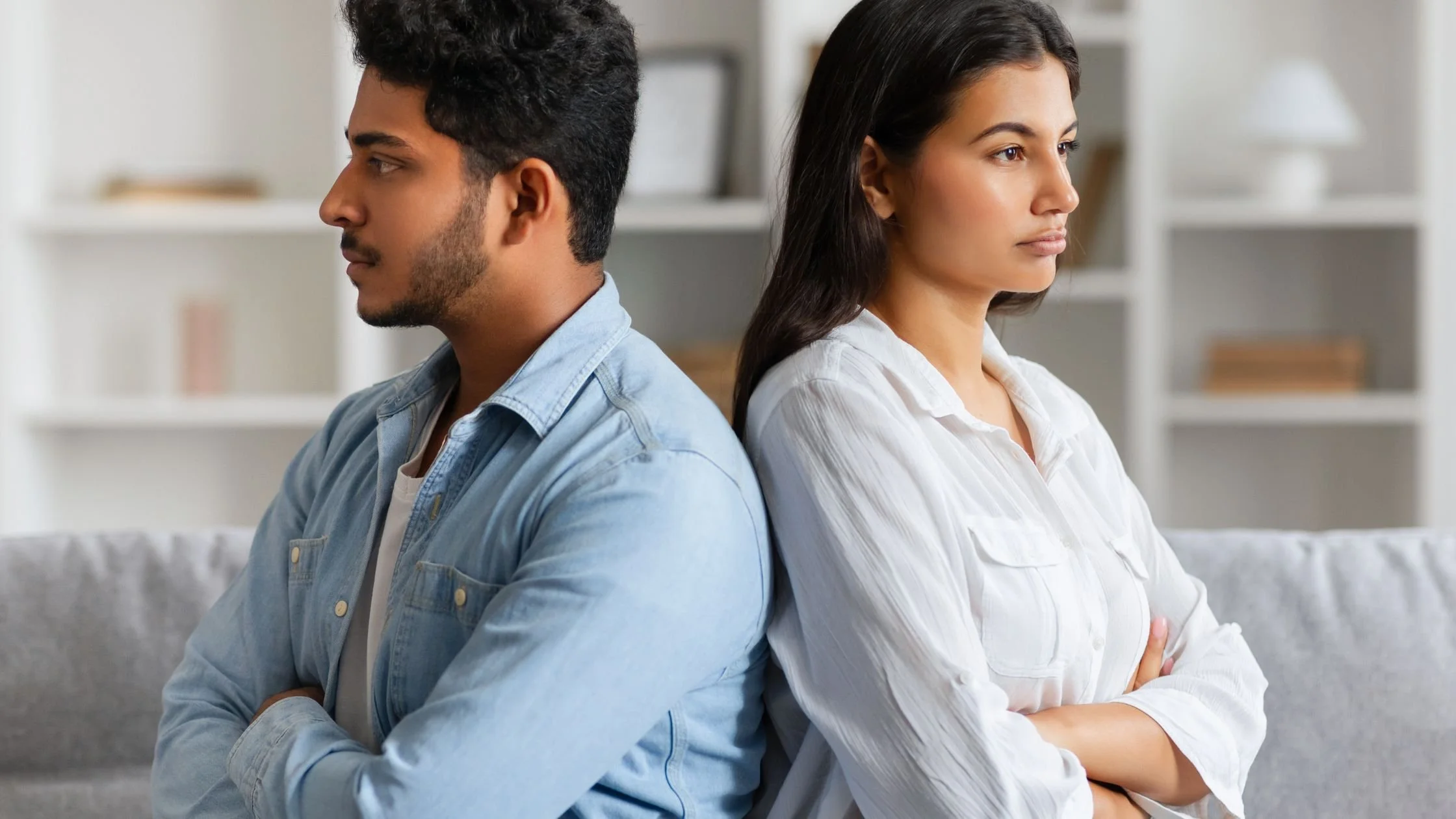 a mand and woman sit back to back, arms crossed, looking upset