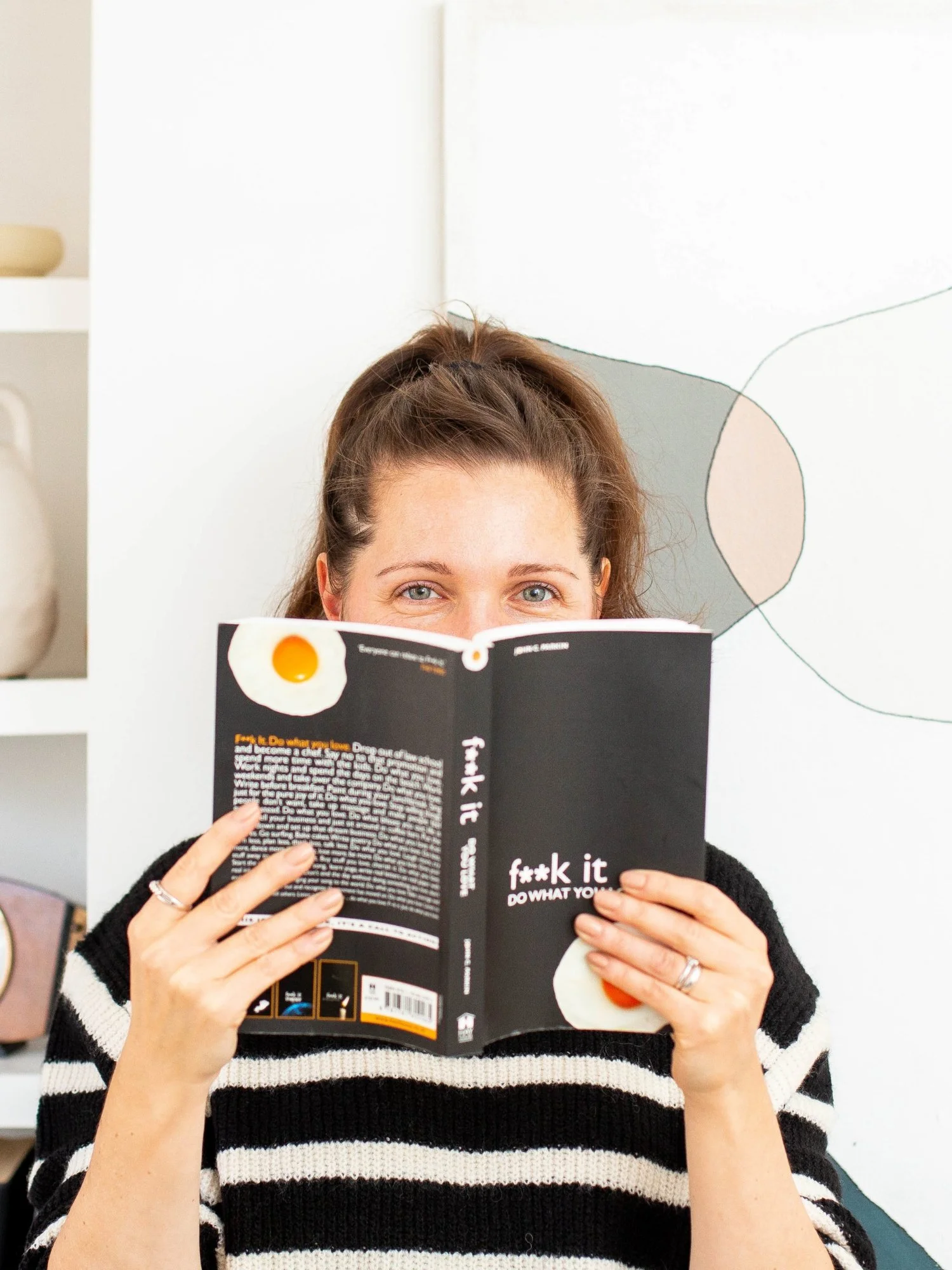 Sam Ferguson creator of Found & Followed course, holding book up to her face with only eyes peeking over the top