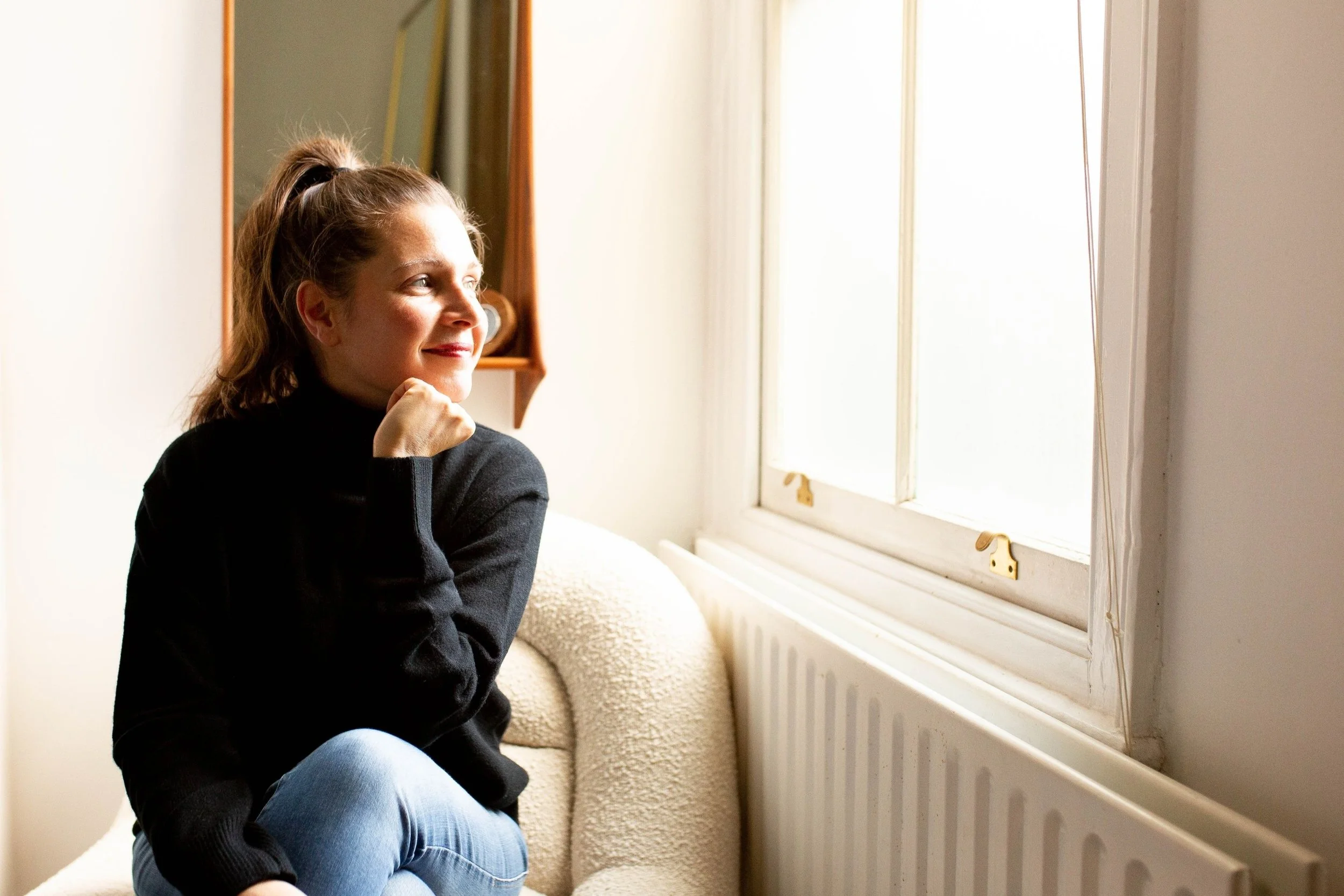 Sam ferguson, owner of Sam Freguson website templates vault. Smiling and looking out of window, in blue jeans and black jumper.