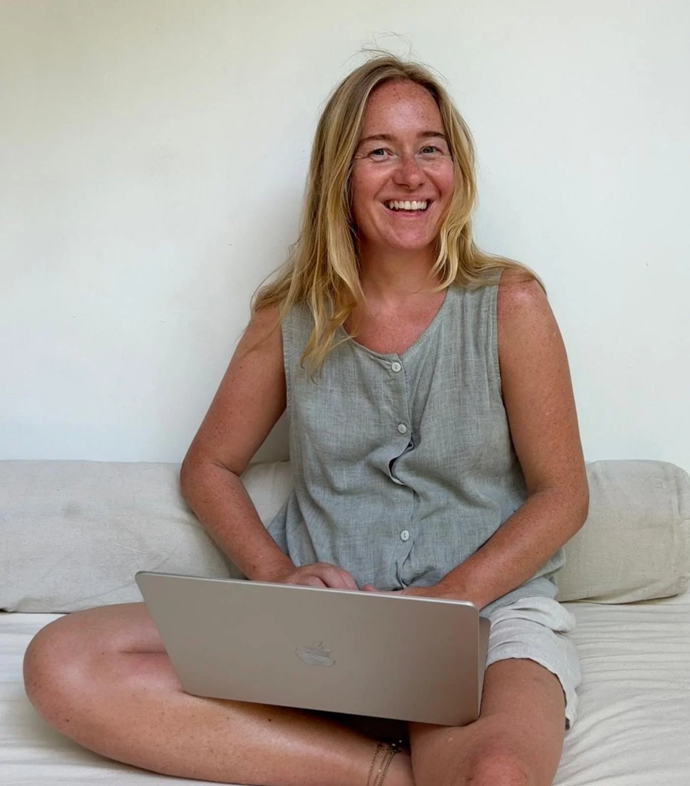 Jo Hurley, Nutritional therapist, sitting on cream sofa, holding laptop and smiling