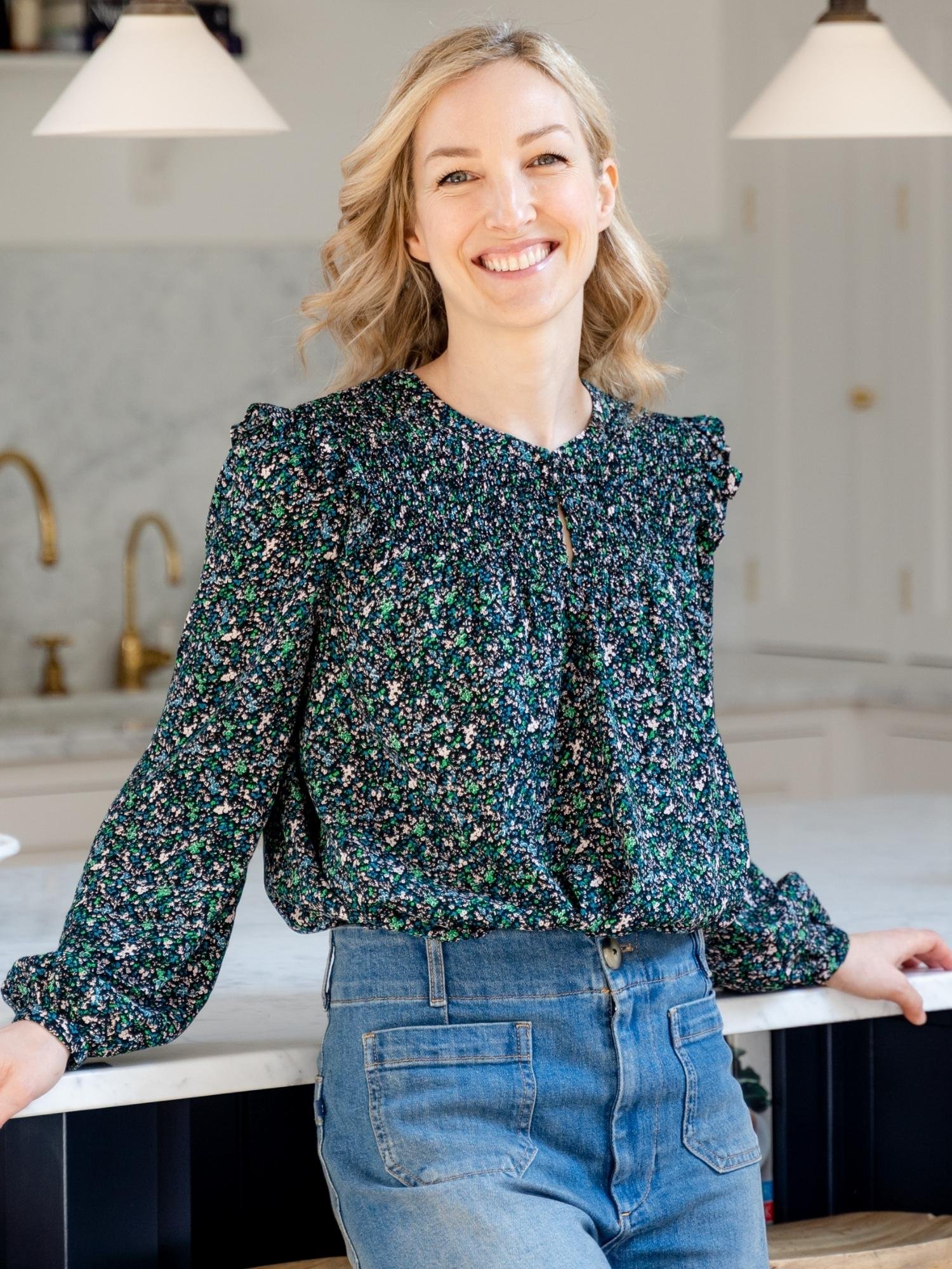 Sandra Greenbank, founder of the Fertility Nutrition Centre and Fertility Specialist in floral top and jeans standing against kitchen counter and smiling