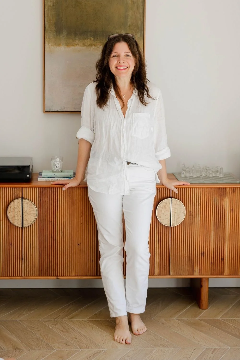 sam ferguson in white outfir, smiling and leaning against a wooden cabinet with record player in view