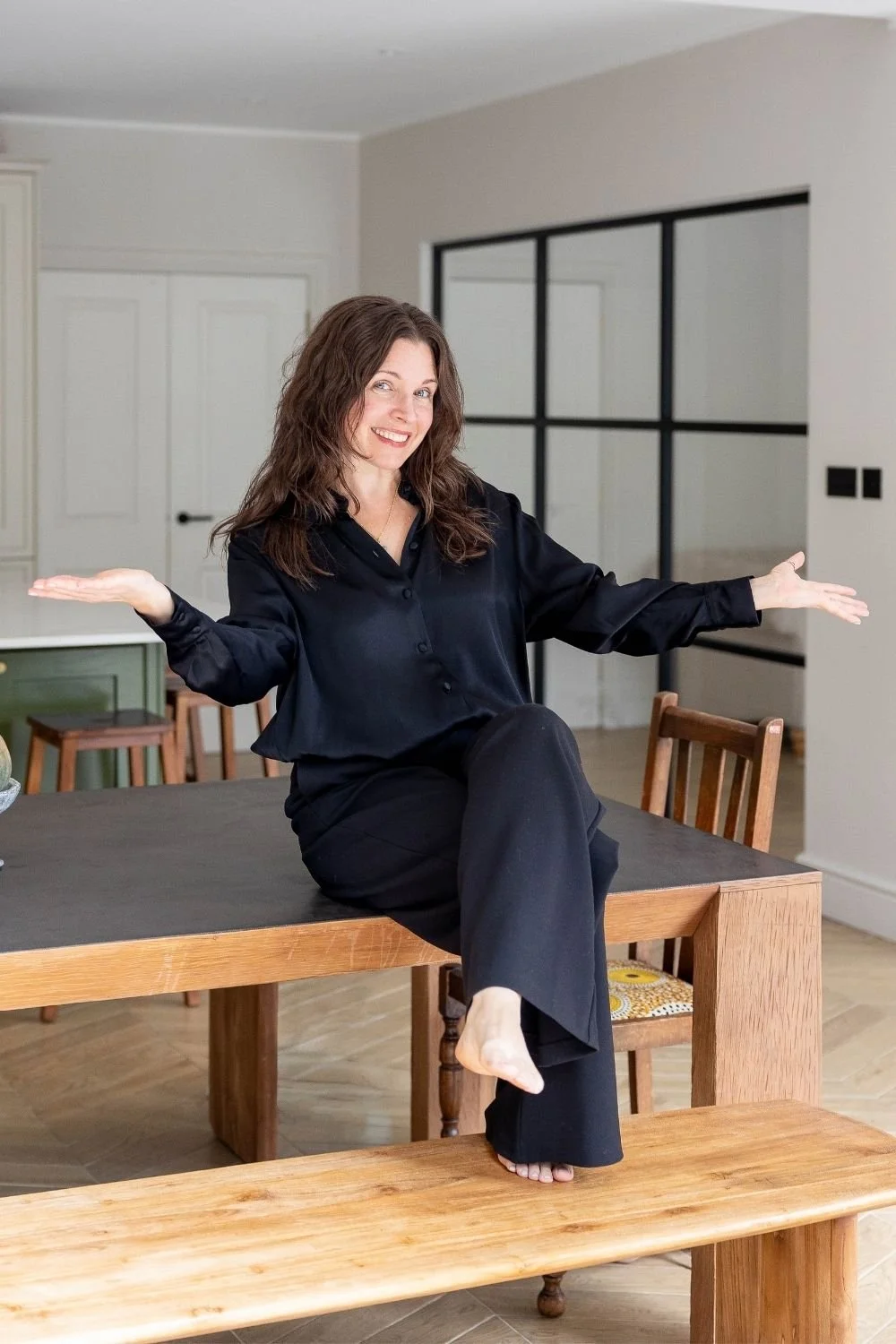 sam ferguson sitting on top of a wooden table, dressed in black and arms outstretched, smiling