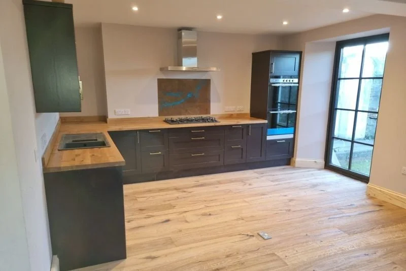 Modern kitchen with dark lower cabinets, wooden countertops, a gas stove, built-in oven, and large glass sliding door leading outside