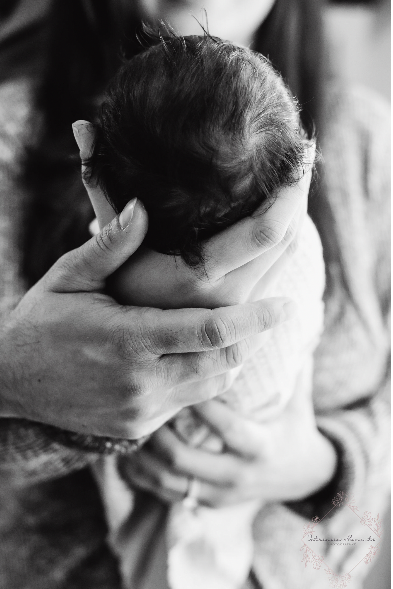 Black and white photo of a baby being cradled by an adult, showing the baby's head and hair.