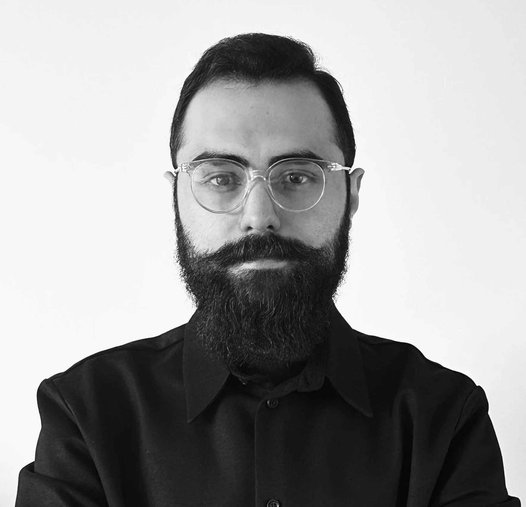 Black and white portrait of a man with glasses and a full beard, wearing a dark collared shirt, against a plain light-colored background.