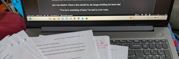 A laptop is open with a pile of papers on the keyboard. The papers have edit marks in read pen.