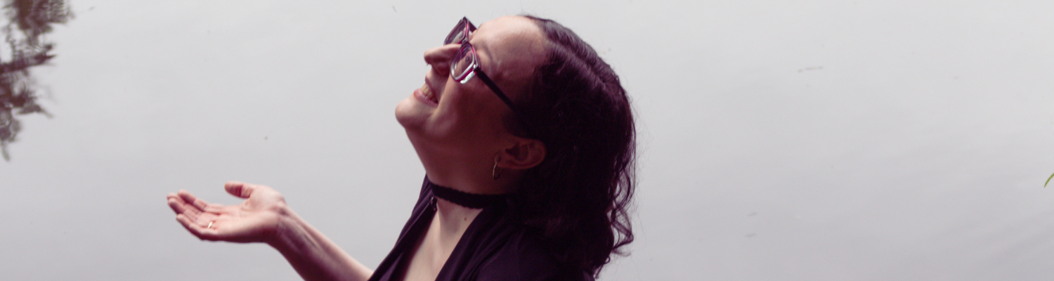 Image of Leani Lopez near water, smiling and looking up a the rain with her hand outstretched