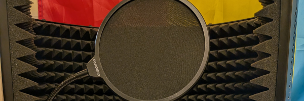 A photo of a pop filter in front of a microphone with the pan flag behind it.