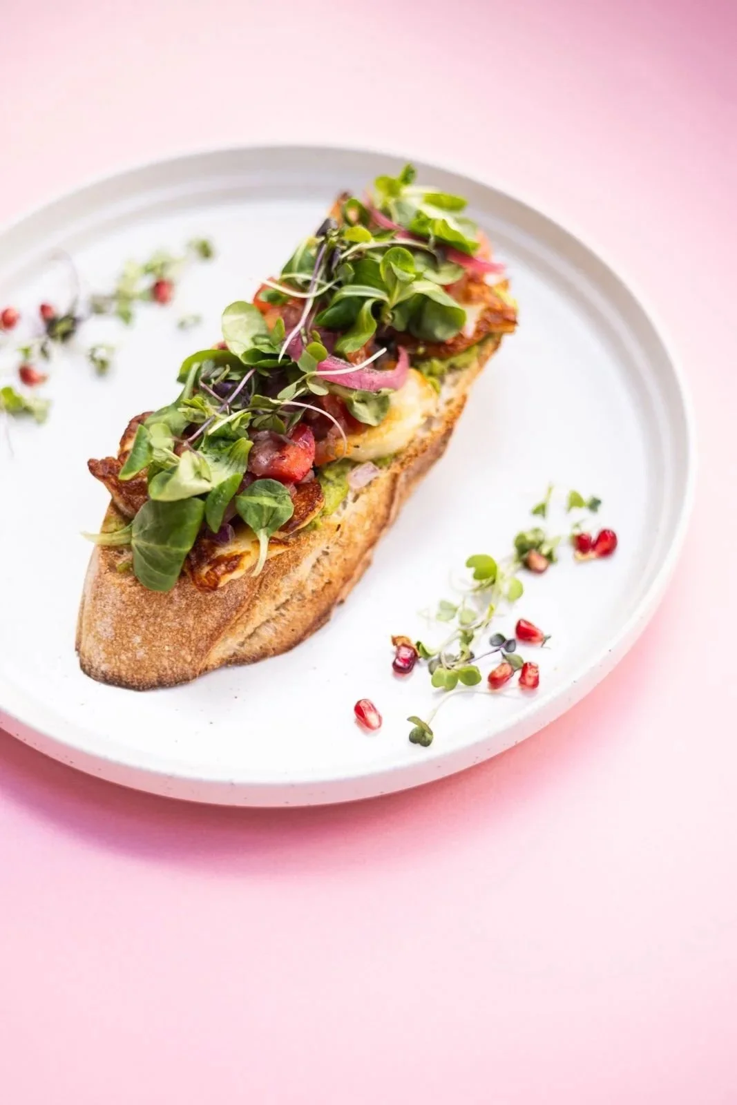 Healthy sandwich on sourdough bread (gluten free available) with microgreens, tomatoes, and pickled onions, pomegranate seeds. Sándwich saludable sobre pan de masa madre (disponible sin gluten) con microvegetales, tomate, cebolla encurtida y semillas
