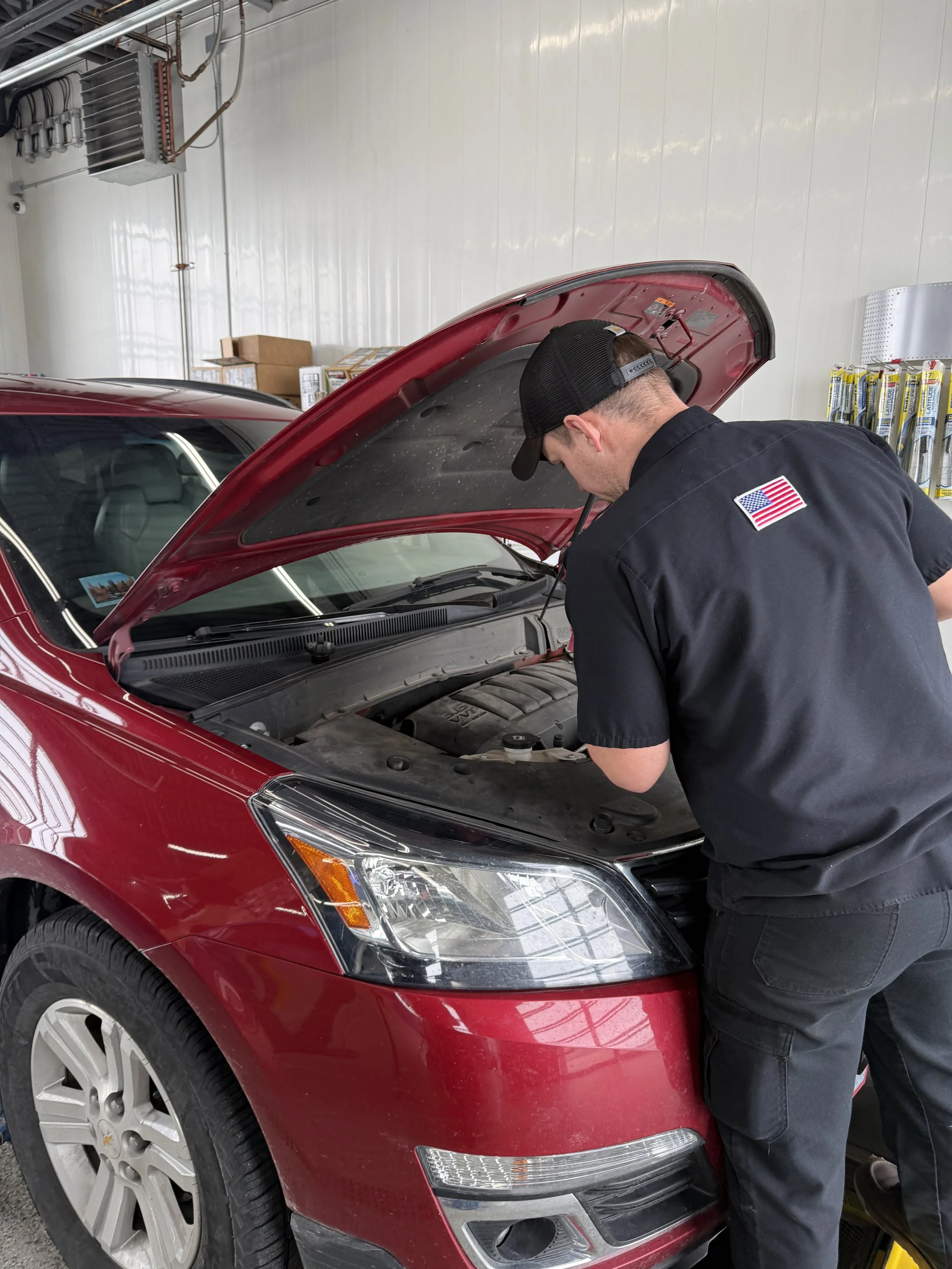 A mechanic inspecting the engine of a red car with its hood open in a garage.