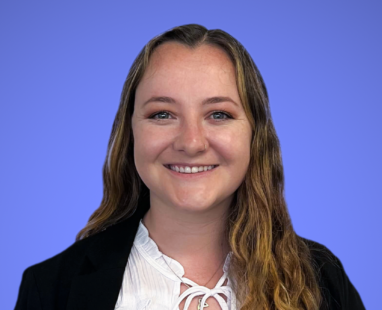 headshot image of a female with brown hair wearing a black blazer and white shirt against a purple background.