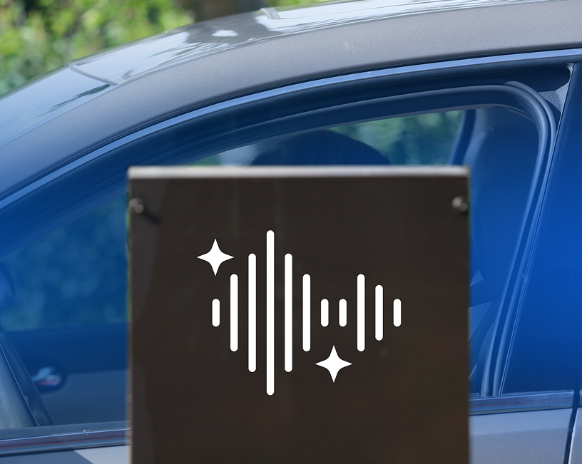 A black sign with a white sound wave graphic and sparkles in front of a blue car window.