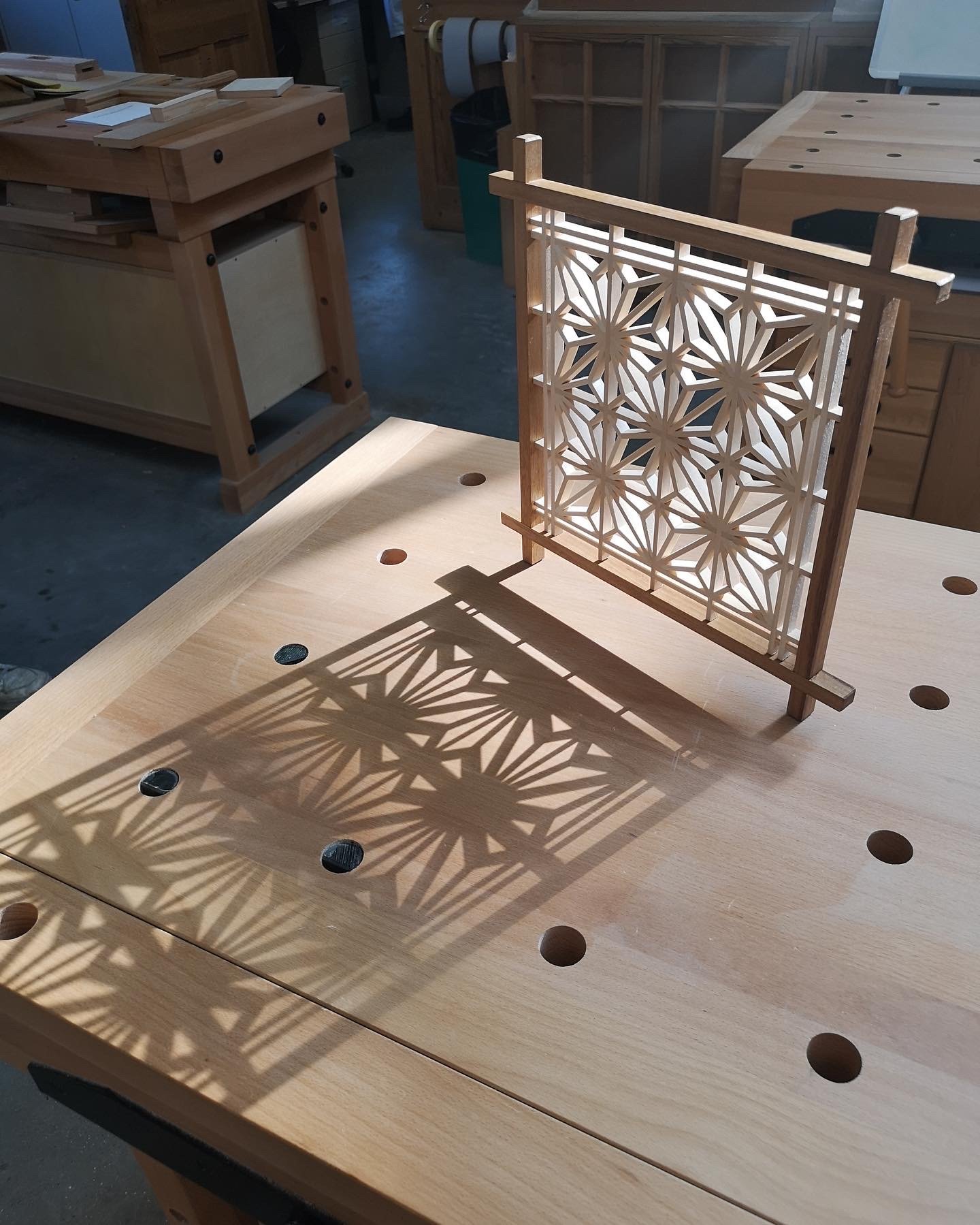 Wooden kumiko panel with geometric pattern casting shadow on workbench.