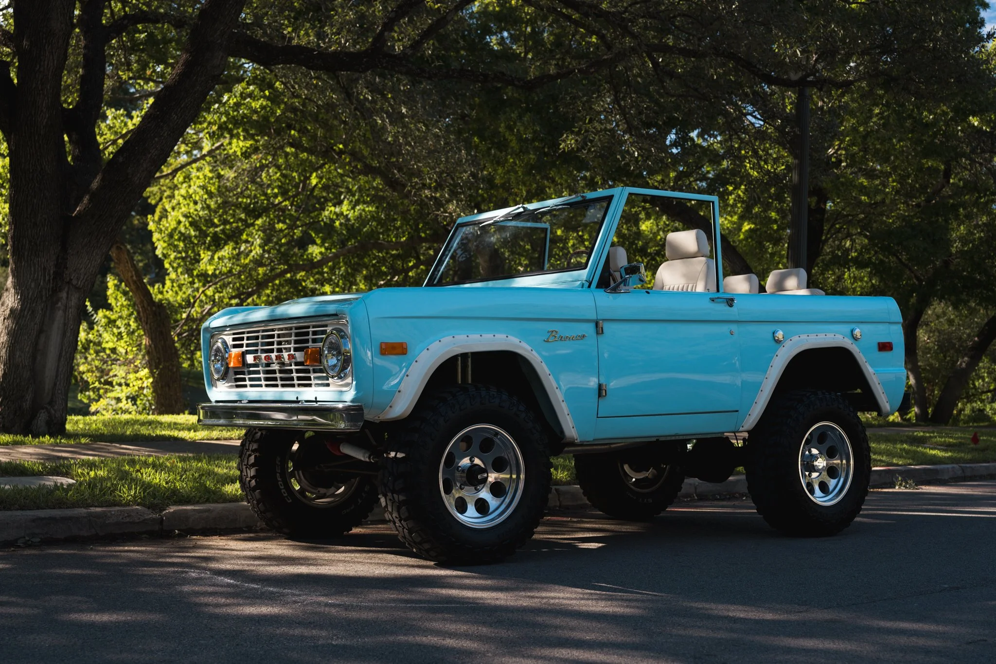 a baby blue 1974 Ford Bronco decorated with flowers in a green park