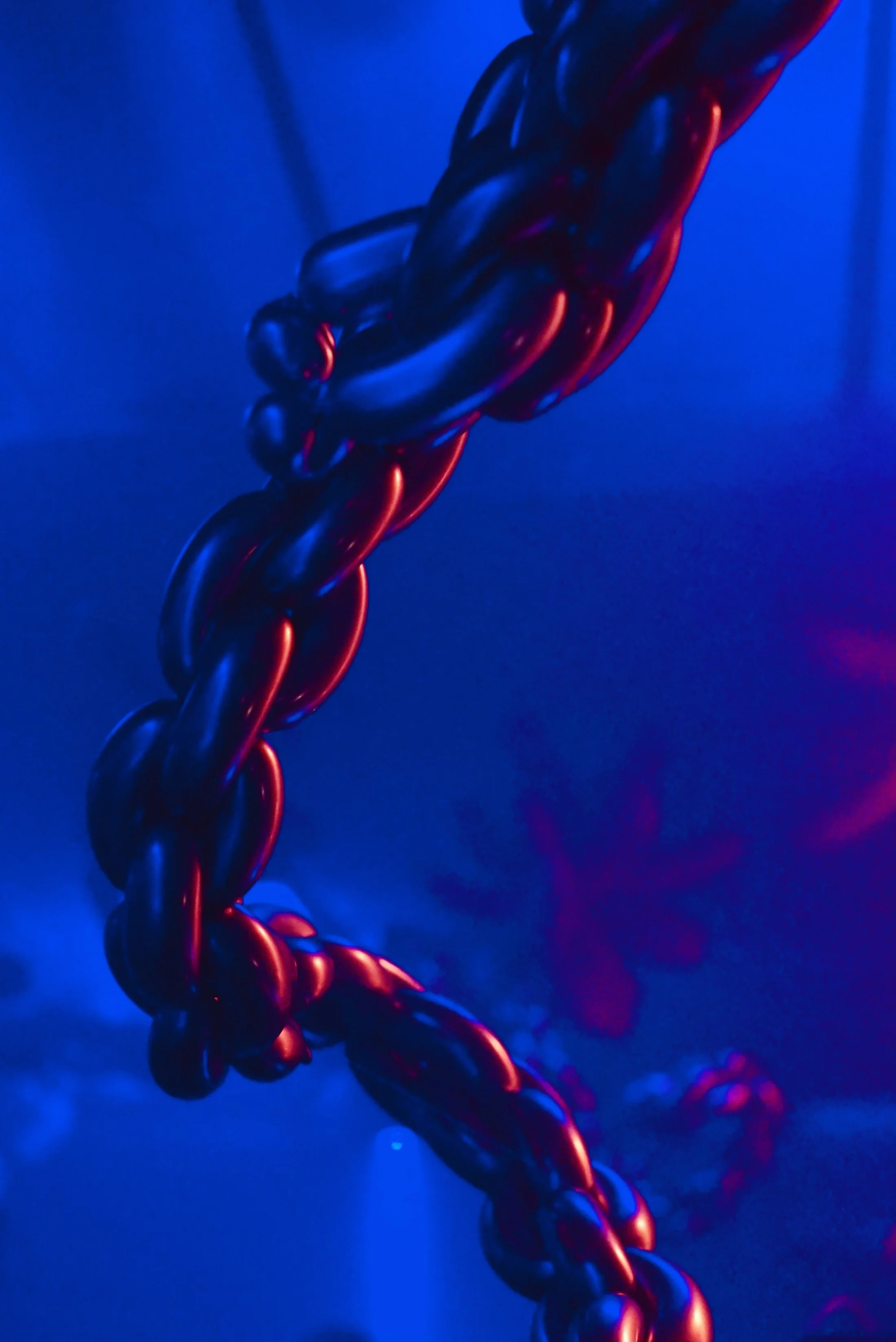 Close-up of a thick, twisted, black metallic chain with a glossy surface, illuminated by red and blue lighting.
