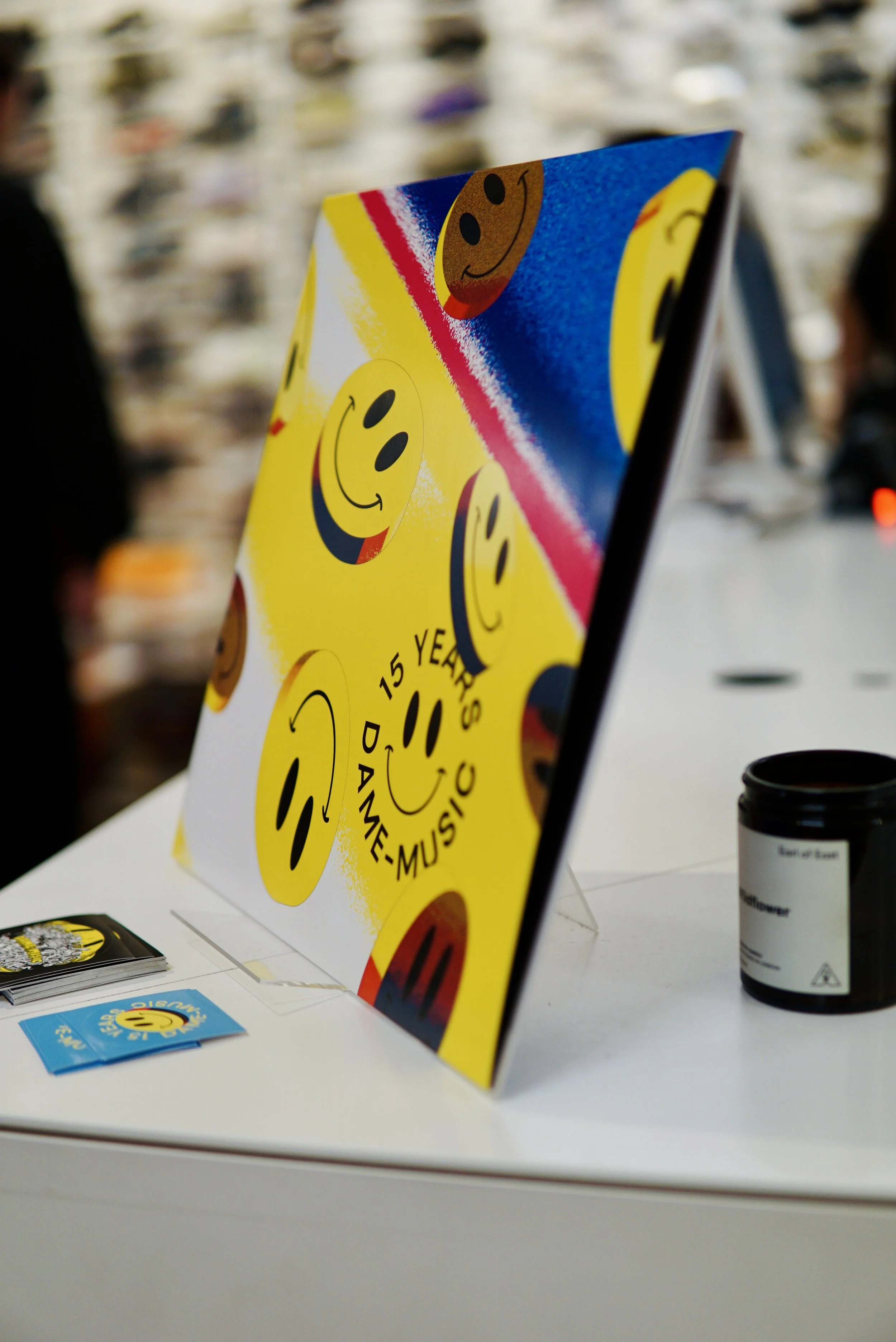 Colorful sign with yellow smiley faces and text celebrating 15 years of dance, music, and fun, set on a white table at an event.