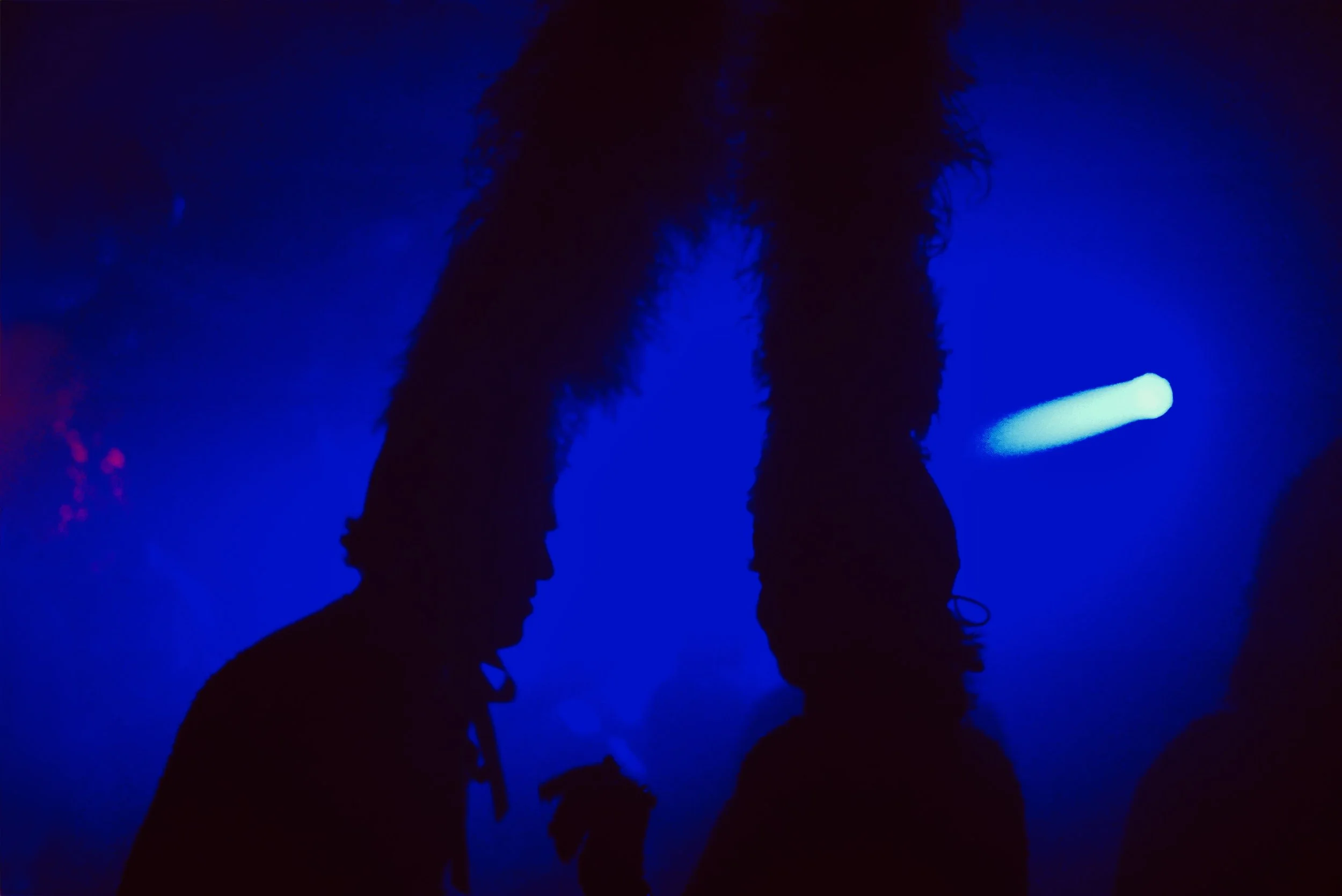 Silhouettes of two people in a dark blue environment, with one person having hair standing up and illuminated by blue light.