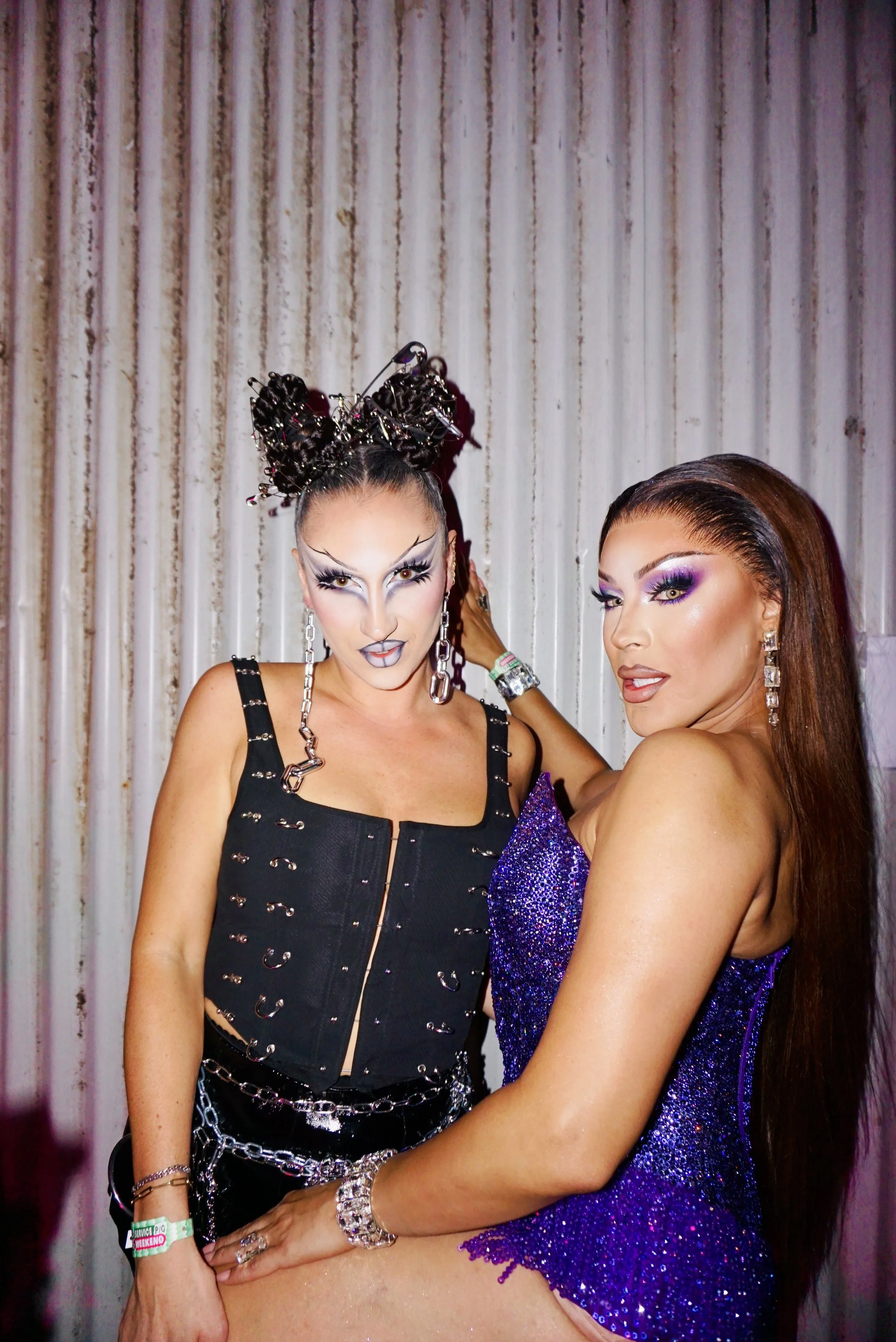 Two women in glamorous costumes posing for the camera at a party or event, with a textured background.