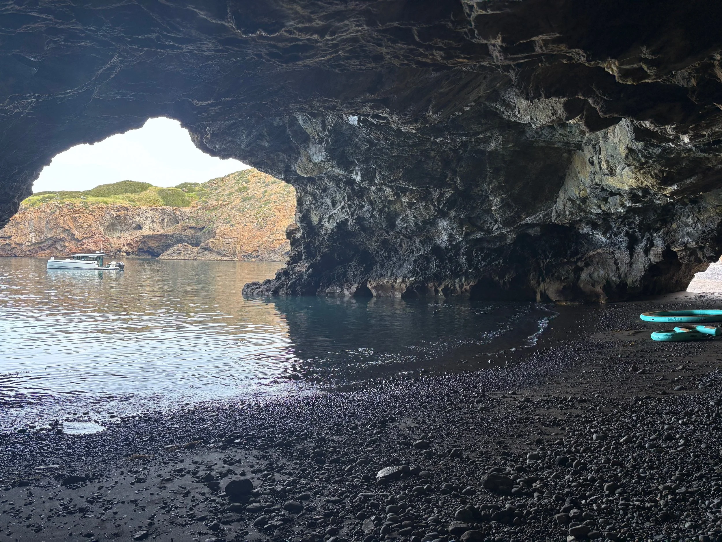 A view from inside a dark cave looking out at the ocean and rocky cliffs with a boat floating on the water.
