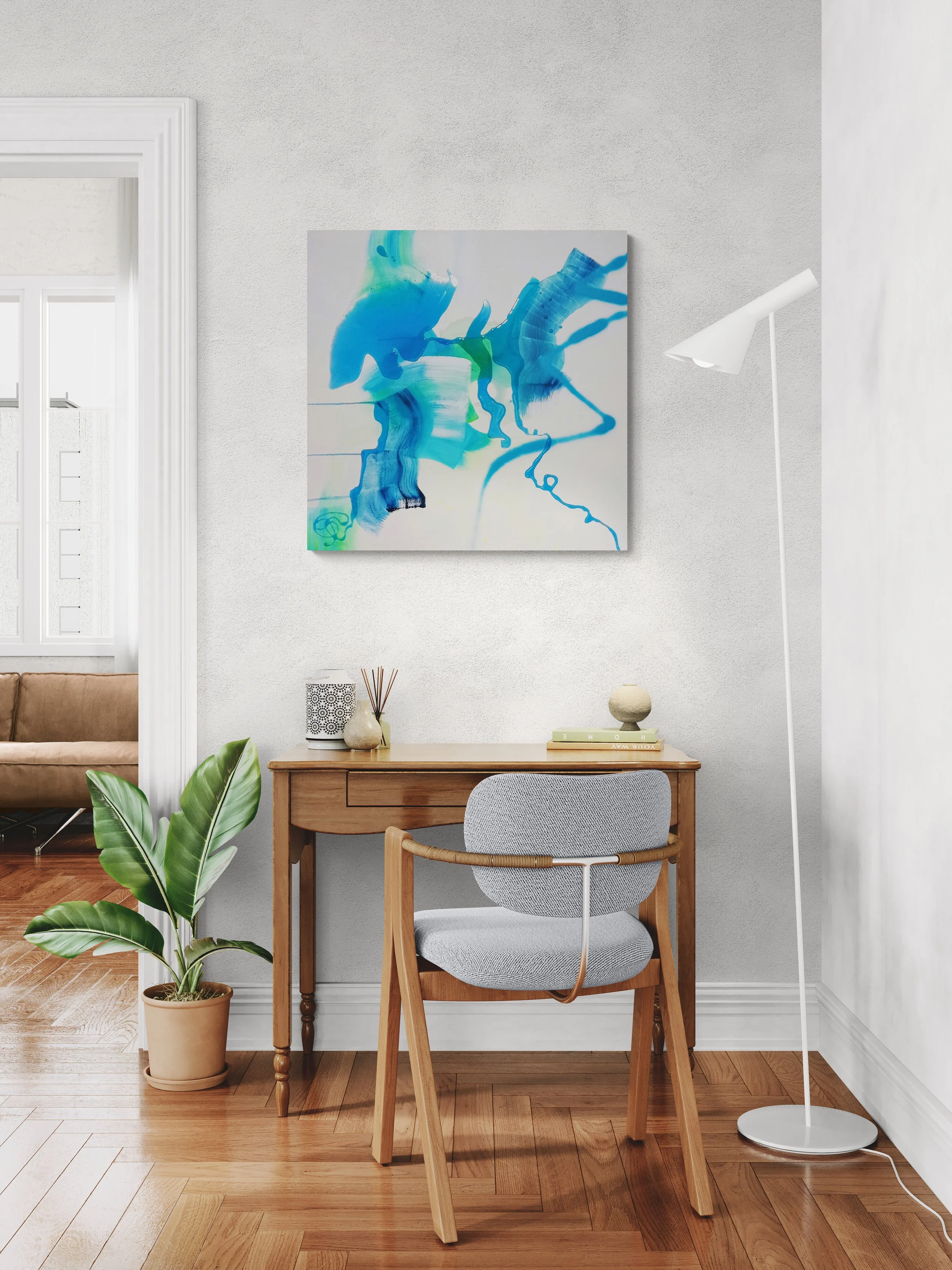 Modern home office setup with wooden desk, grey armchair, white floor lamp, potted plant, with an abstract blue and green painting on the wall.