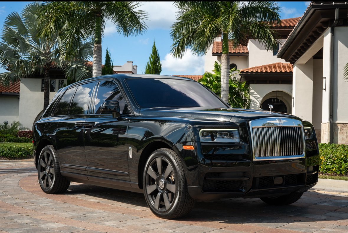 A black luxury SUV parked in a driveway in front of a house with palm trees.