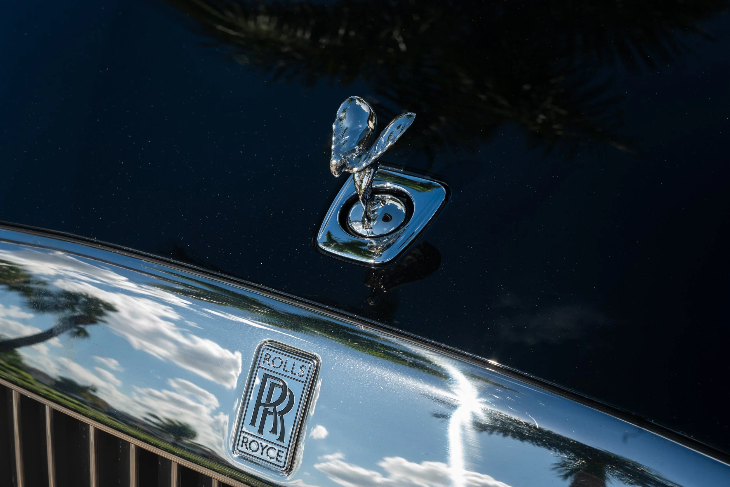 Close-up of a black Rolls Royce car hood with the Spirit of Ecstasy hood ornament and a chrome grille with the Rolls Royce emblem.